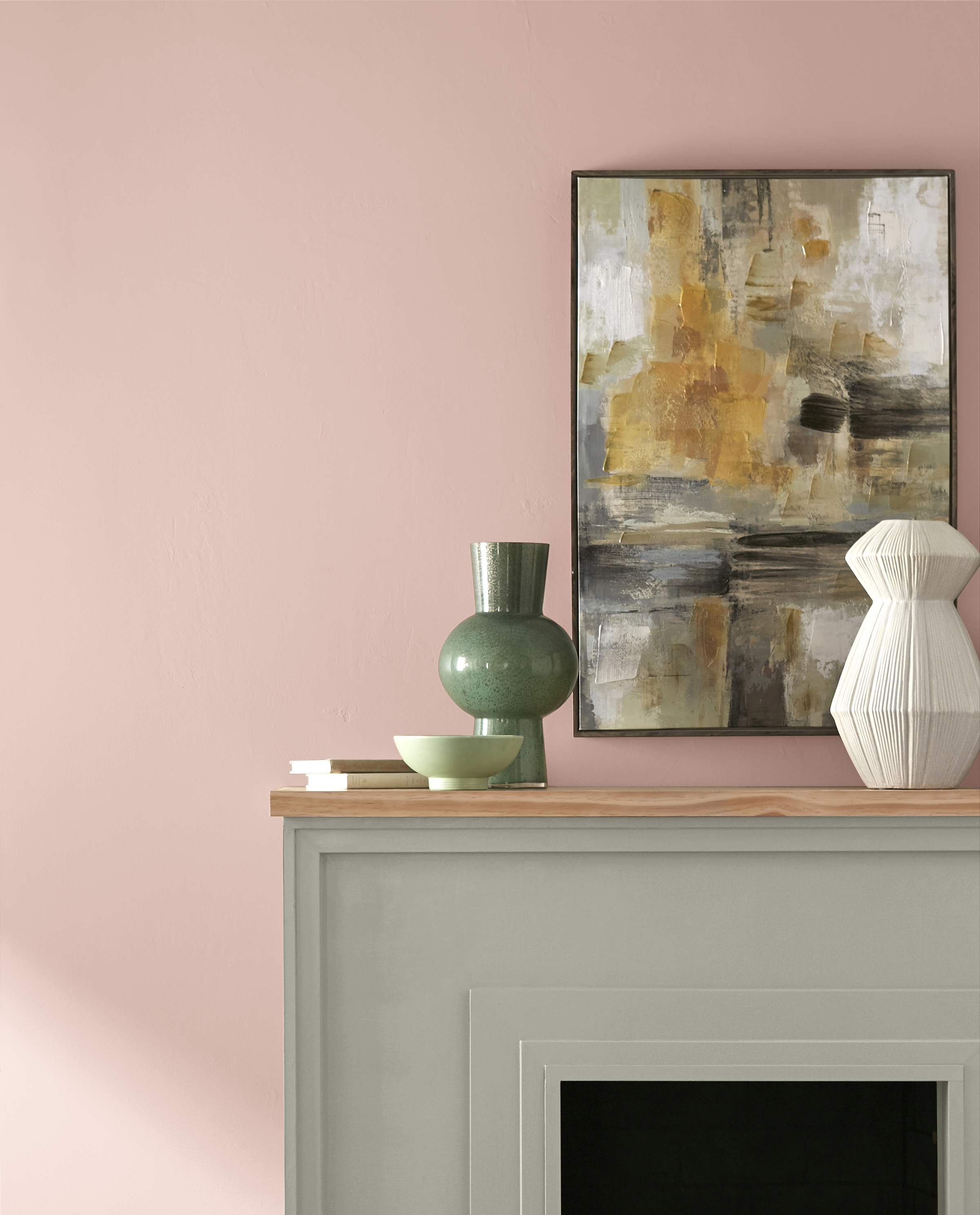 A close up photo of a living room wall featuring a fireplace, the wall is painted in a light pink and fireplace mantle is painted in a grayed- green paint color. 