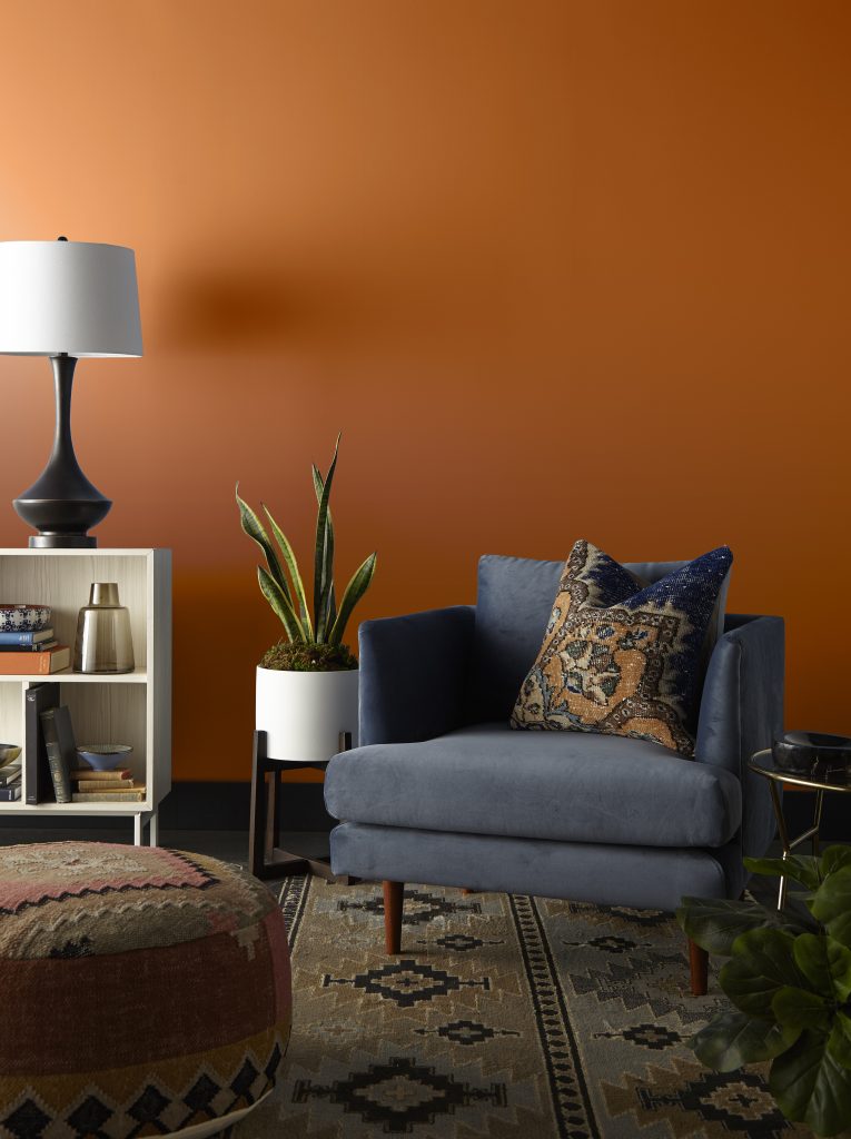 A seating nook area with walls painted in a bright orange colour, styled with a comfy chair, plants, and a small bookshelf