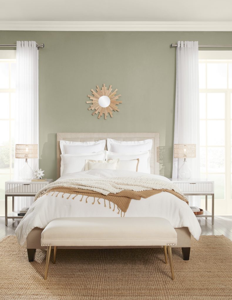 A bedroom with walls painted in a grey-green colour styled with neutral bedding and white curtains