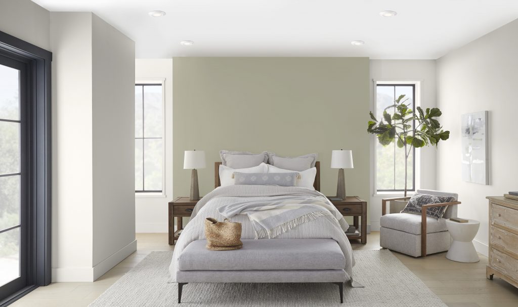 A bright and airy bedroom with the wall behind the bedroom painted in a light grey-green colour