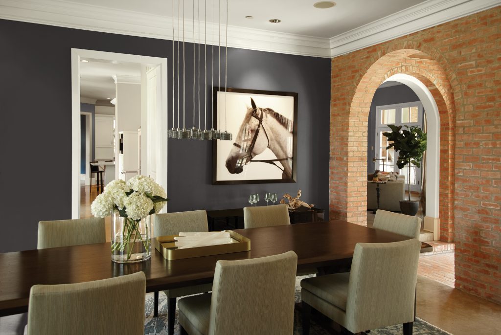 A dining room with a brick accent wall to the right and walls painted in black, styled with western décor 