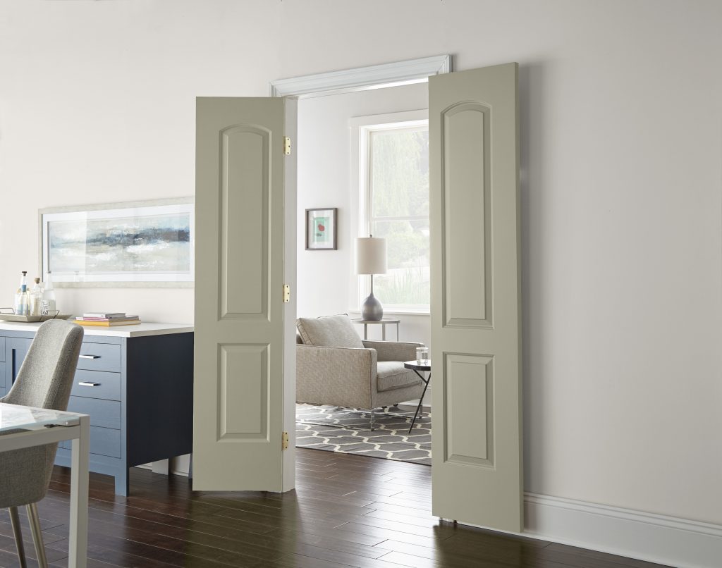 A glimpse into a living room through double doors that are painted in a light grey-green colour