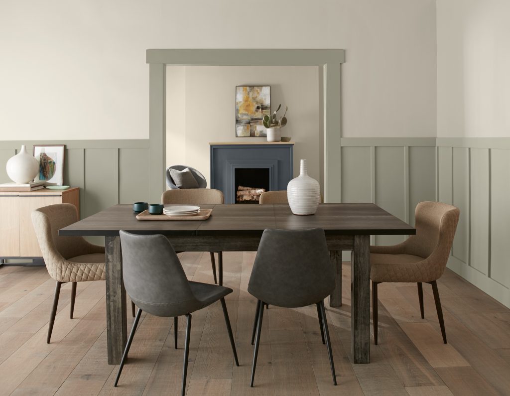 A spacious dining room with wainscotting and trim painted in a light grey-green colour
