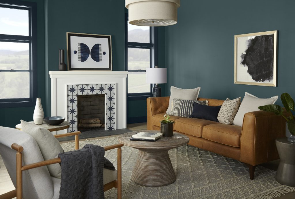 A living room with walls painted in a deep blue-green colour, styled with a leather sofa, coffee table, and cushioned chair