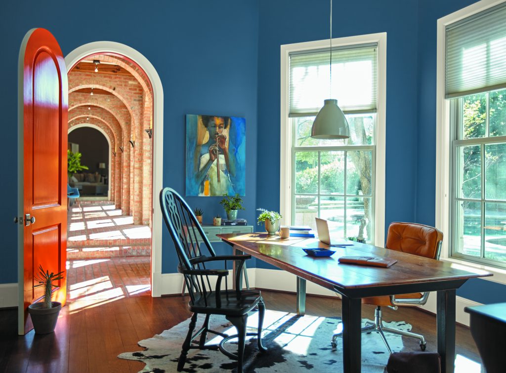 A home office space with blue walls, styled with a wooden table, mismatched chairs, and western décor 