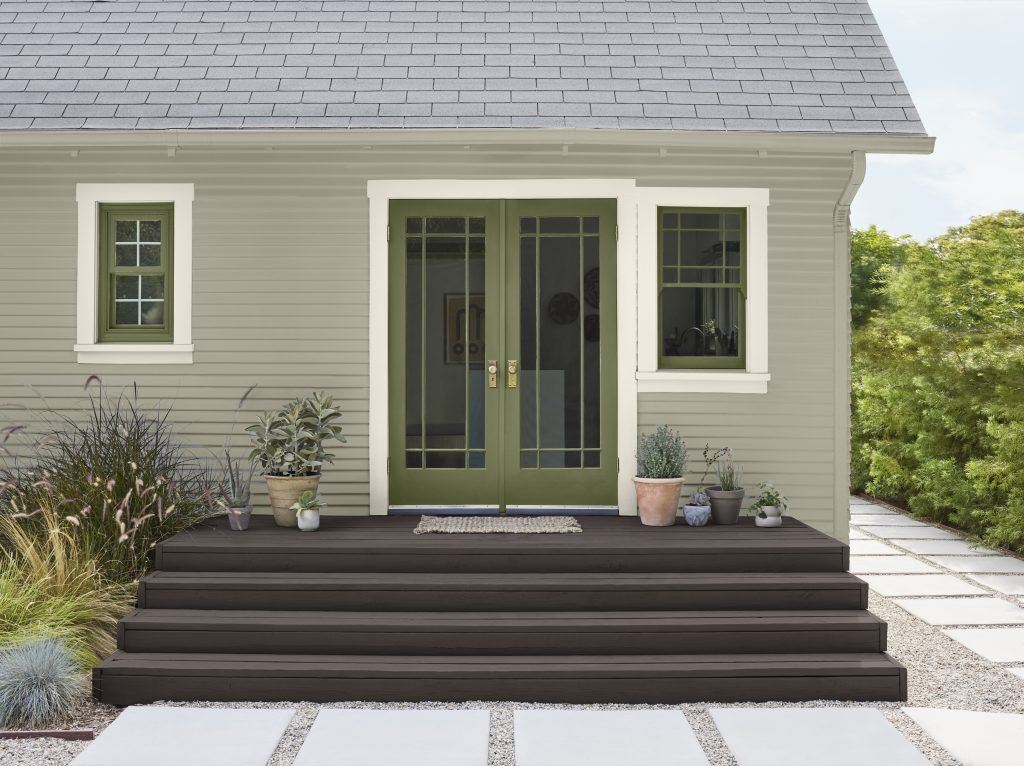 A small house exterior with grey-green siding and a green double door
