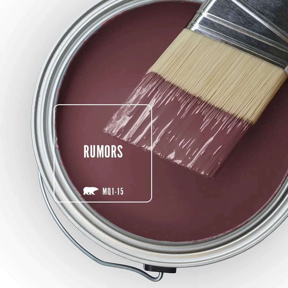 The top view of an open can filled with red paint, the colour’s name is Rumors. A paintbrush with bristles coated in the same maroon paint rests on top of the can, partially over the edge. 