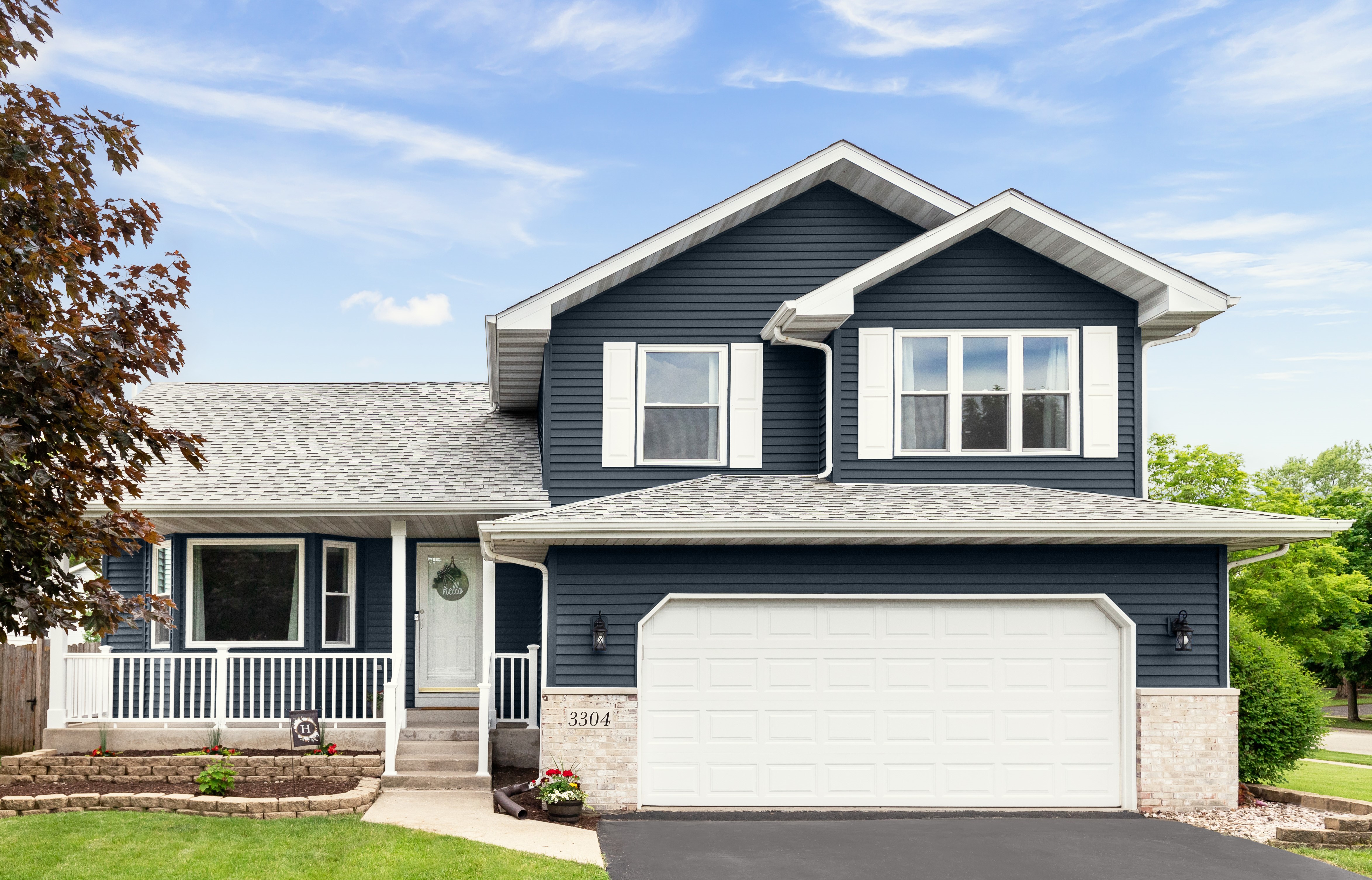 A two-story American Craftman Style home with a dark blue facade and white trim. The colour used on the siding is Midnight Blue. The house features a large white garage door, a front porch with white railings, and three upper-level windows with white frames.