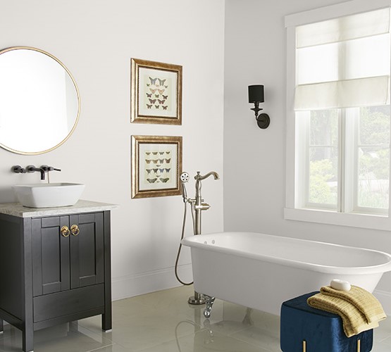 Traditional bathroom featuring white walls and ceiling, creating a clean and airy atmosphere. Centered in the space is a classic freestanding bathtub, positioned below a large window with white trim and panes that allow natural light to flood in.