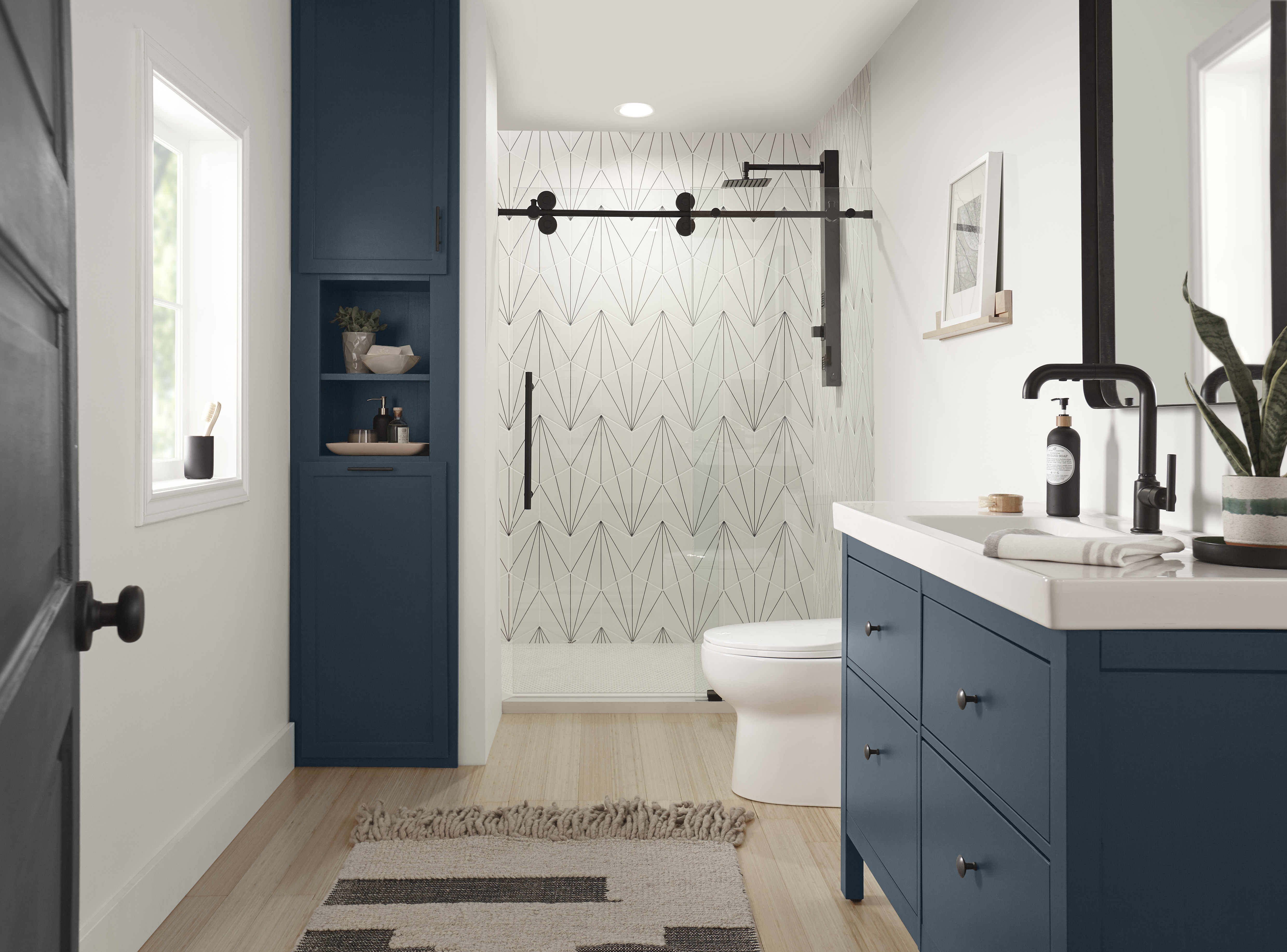 A modern bathroom featuring blue accents, including a Midnight Blue door partially open on the left. A large vanity cabinet in the same shade of blue with drawers and cupboard space. The wall behind the toilet and shower area is accented with a geometric shower tile.