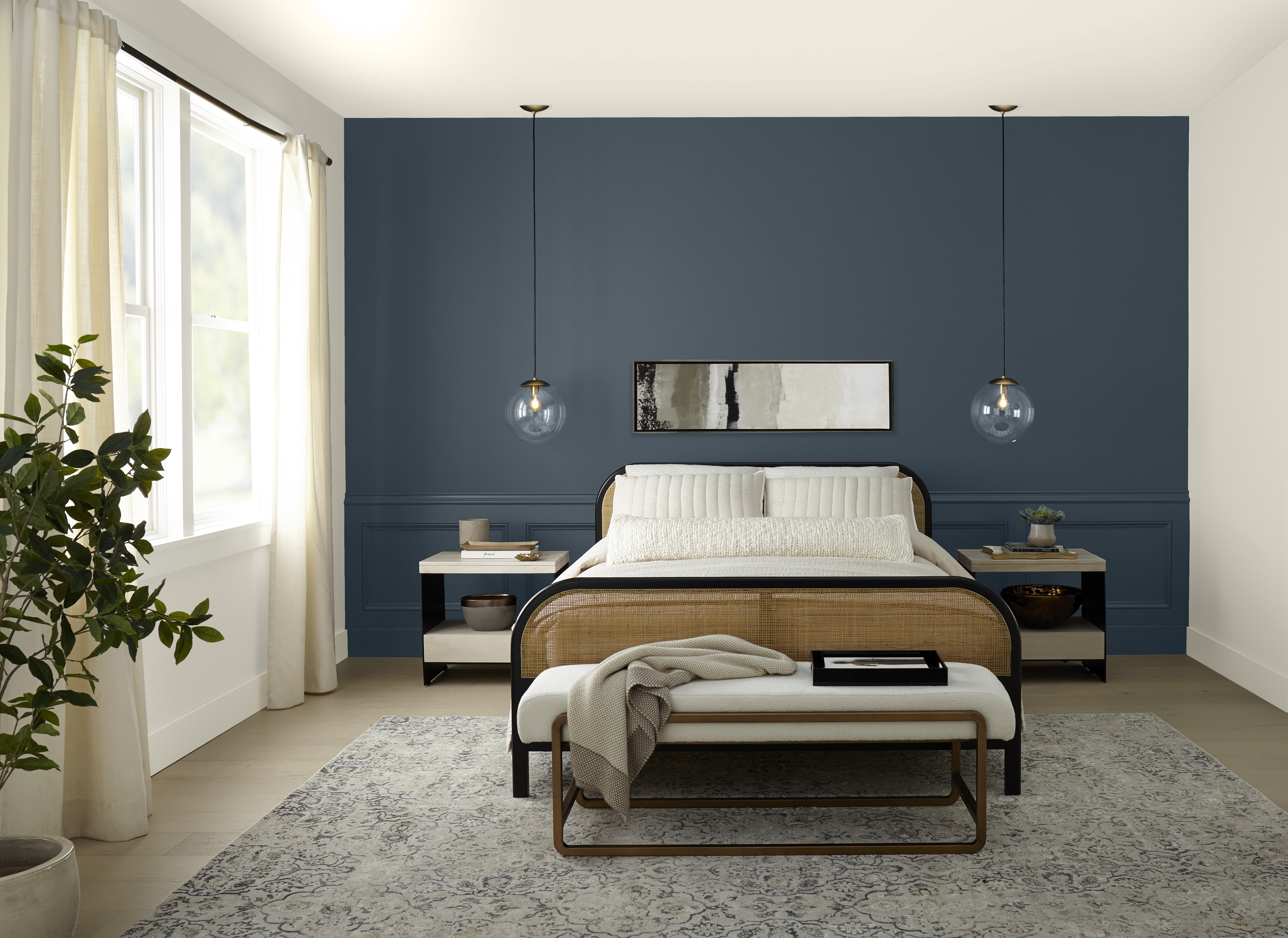 A bedroom featuring a deep blue wall behind the headboard. The wall is adorned with two hanging pendant lights on either side of an abstract black and white artwork centered above the headboard. The blue provides a rich, calming backdrop to the room’s neutral colour palette.