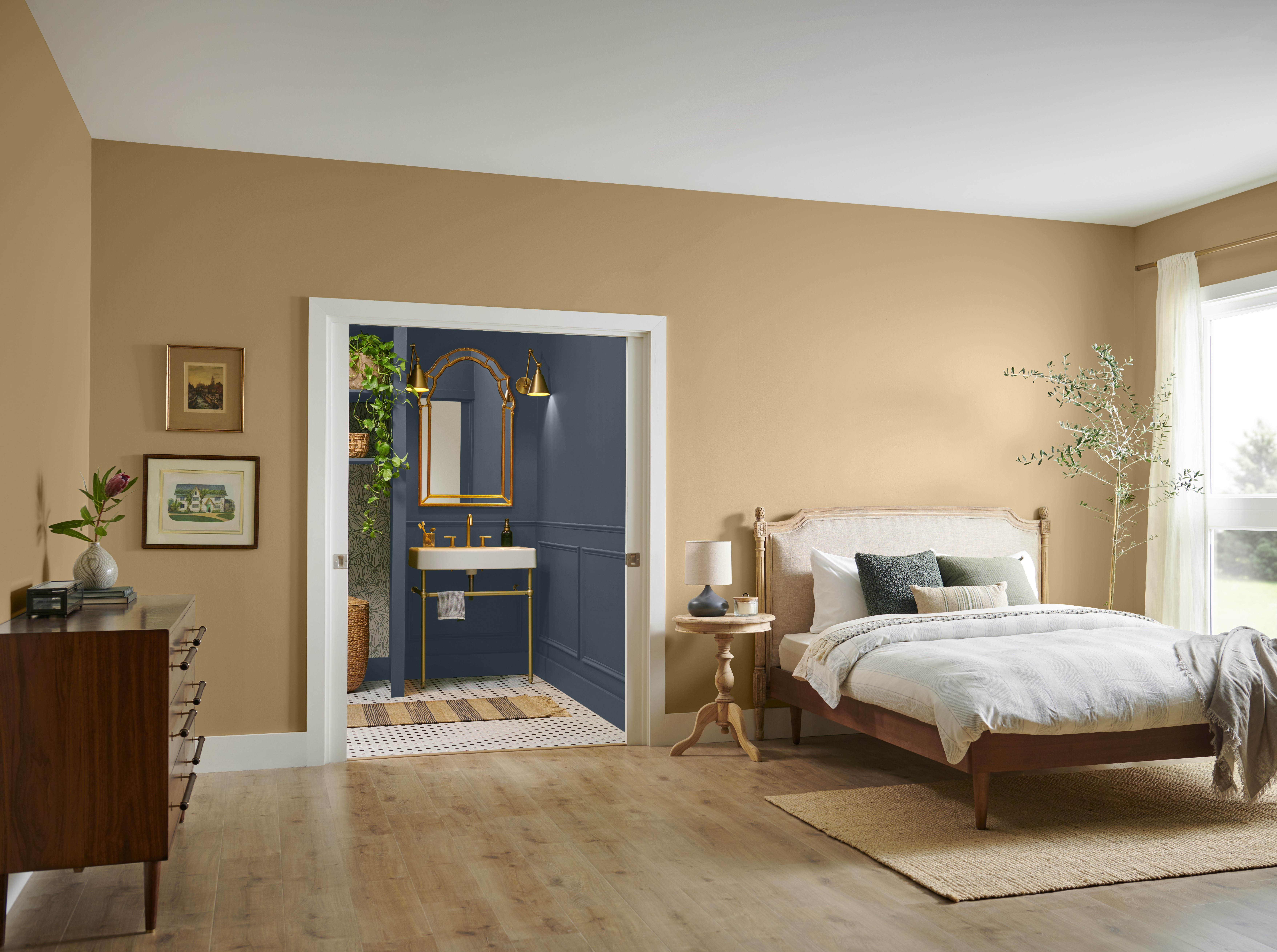 A room with walls painted in Crepe, a warm, inviting tone. The trim is in Whipped Cream, a soft white. The bathroom features Midnight Blue, providing a striking contrast, the space is accented with gold or brass fixtures and greenery, enhancing the luxurious retreat feel.