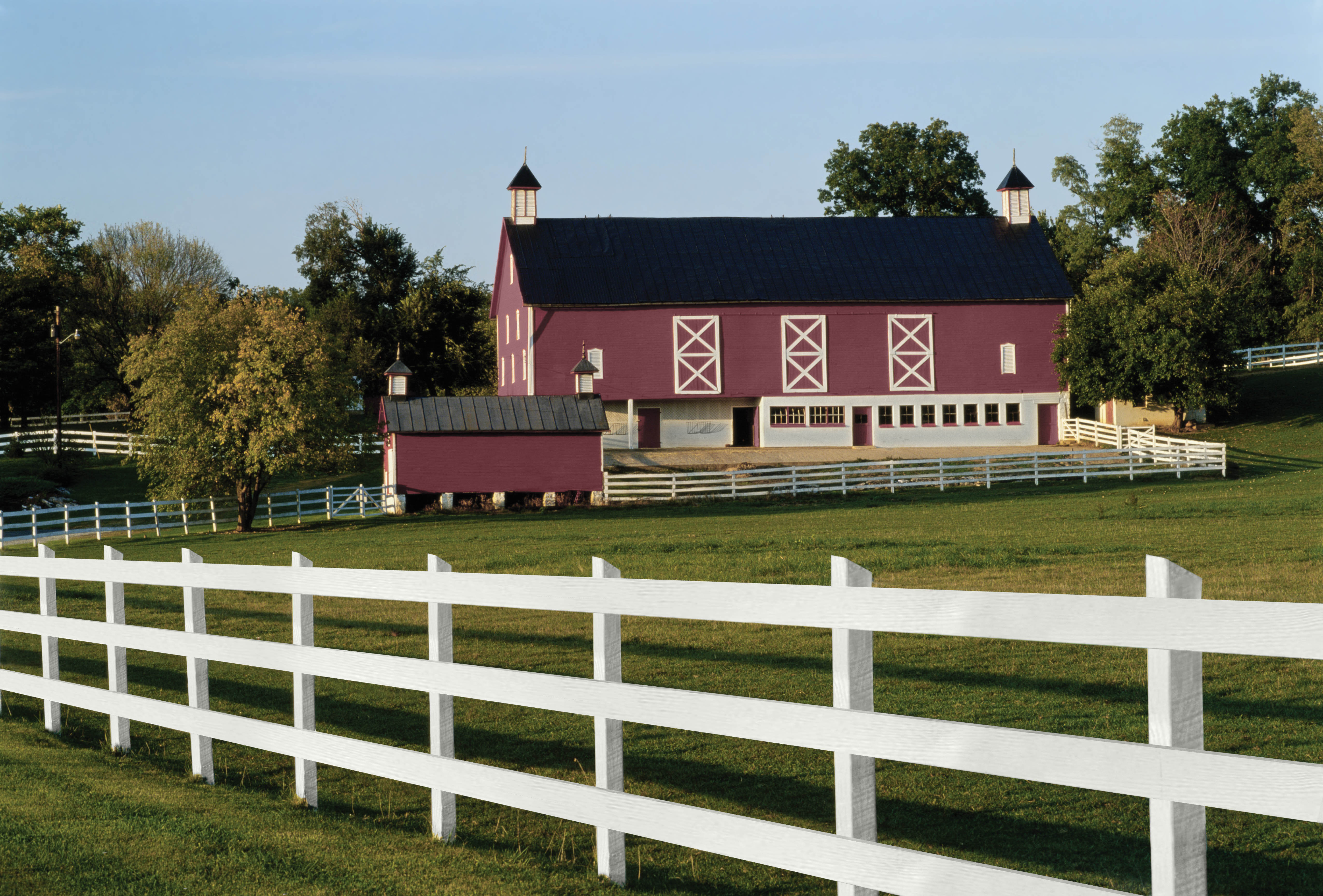 A barn style home painted in a red hue with white trim and picket fence.