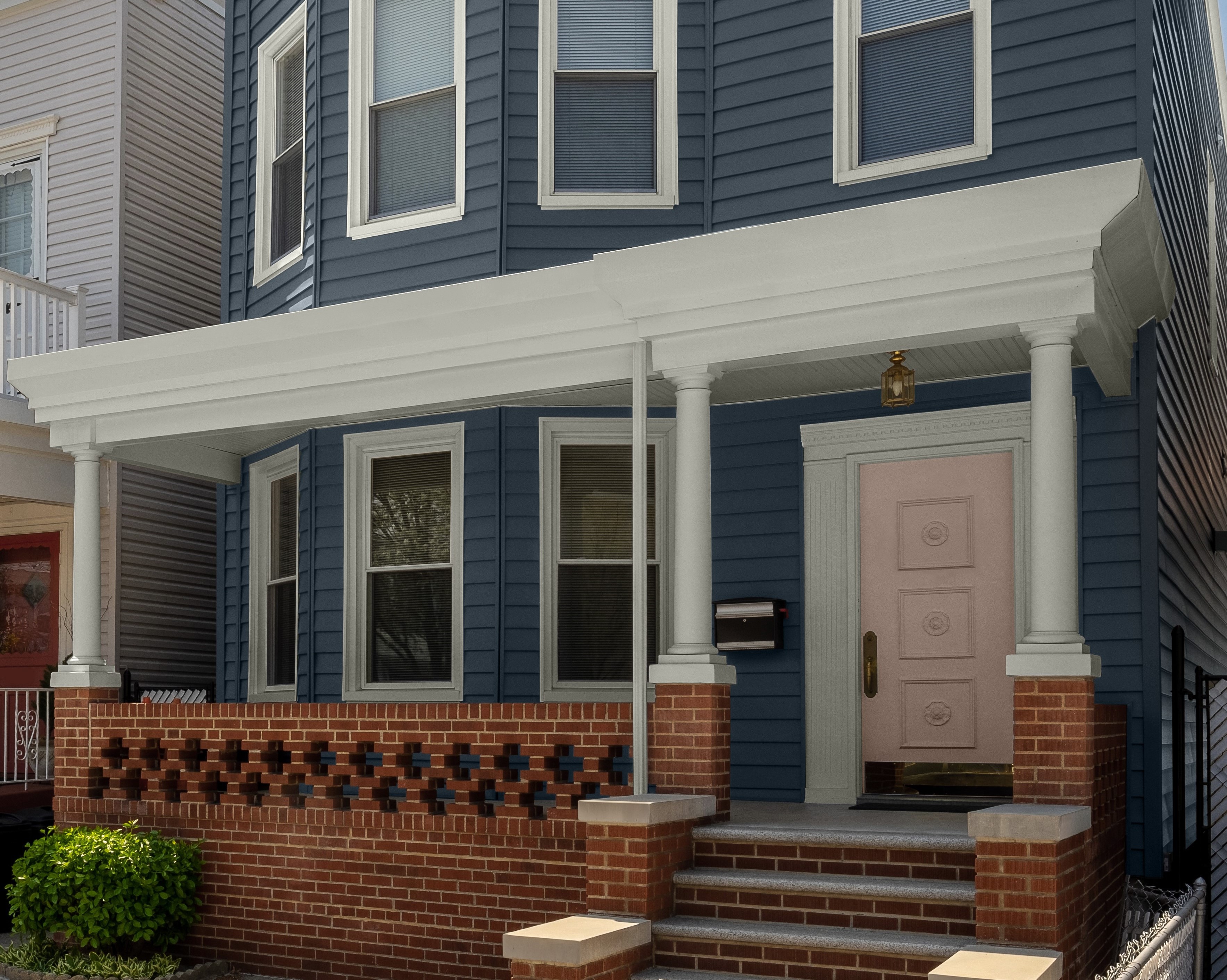 A two-story house featuring Midnight blue siding. The foundation and porch are made of red brick. The trim is painted in Whisper White, and the door is a light pastel tone called Seaside Villa.