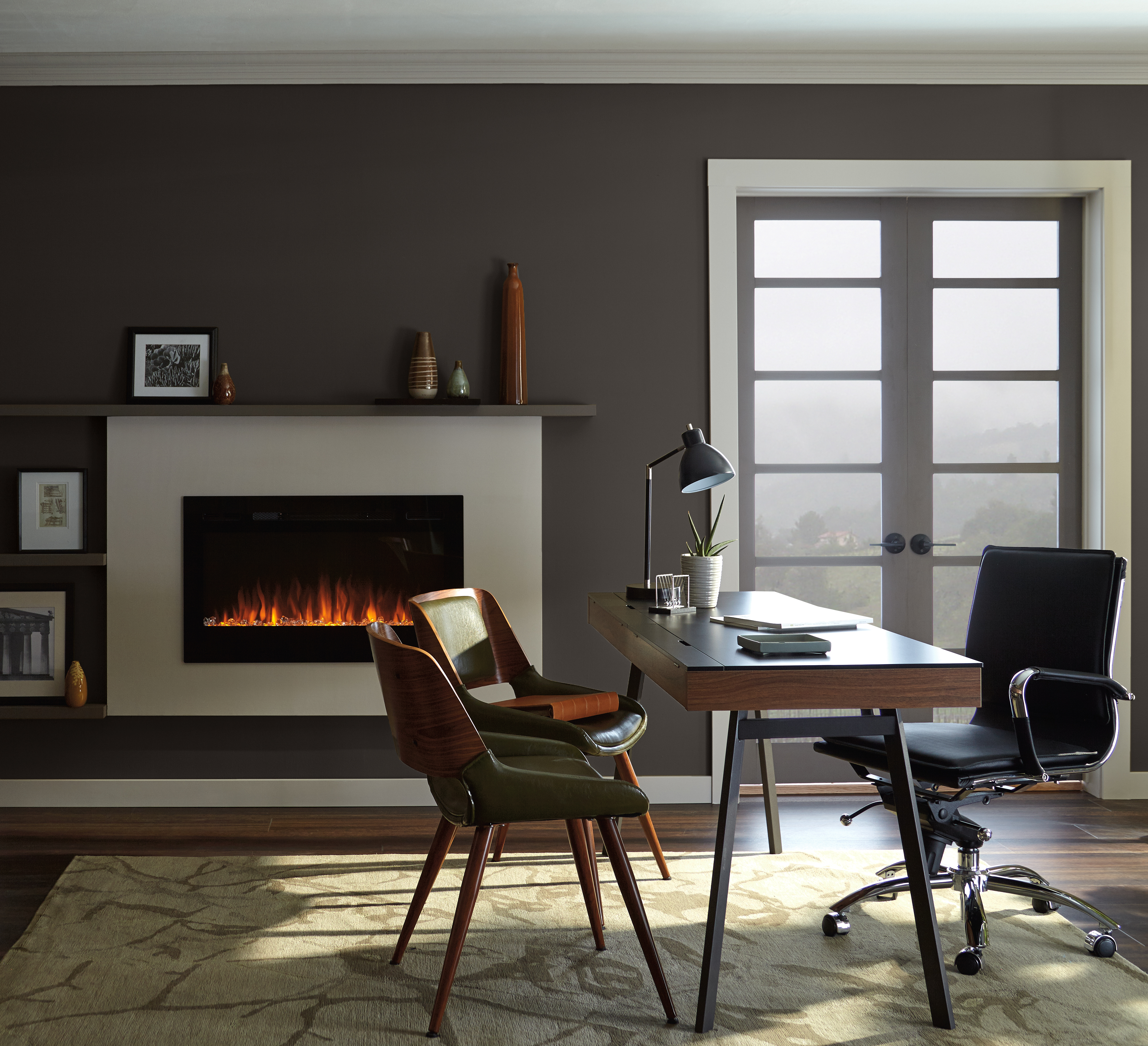 A home office with a fireplace feature and dark brown colour on the walls, the dark tone nicely blends with the view to the outdoors.