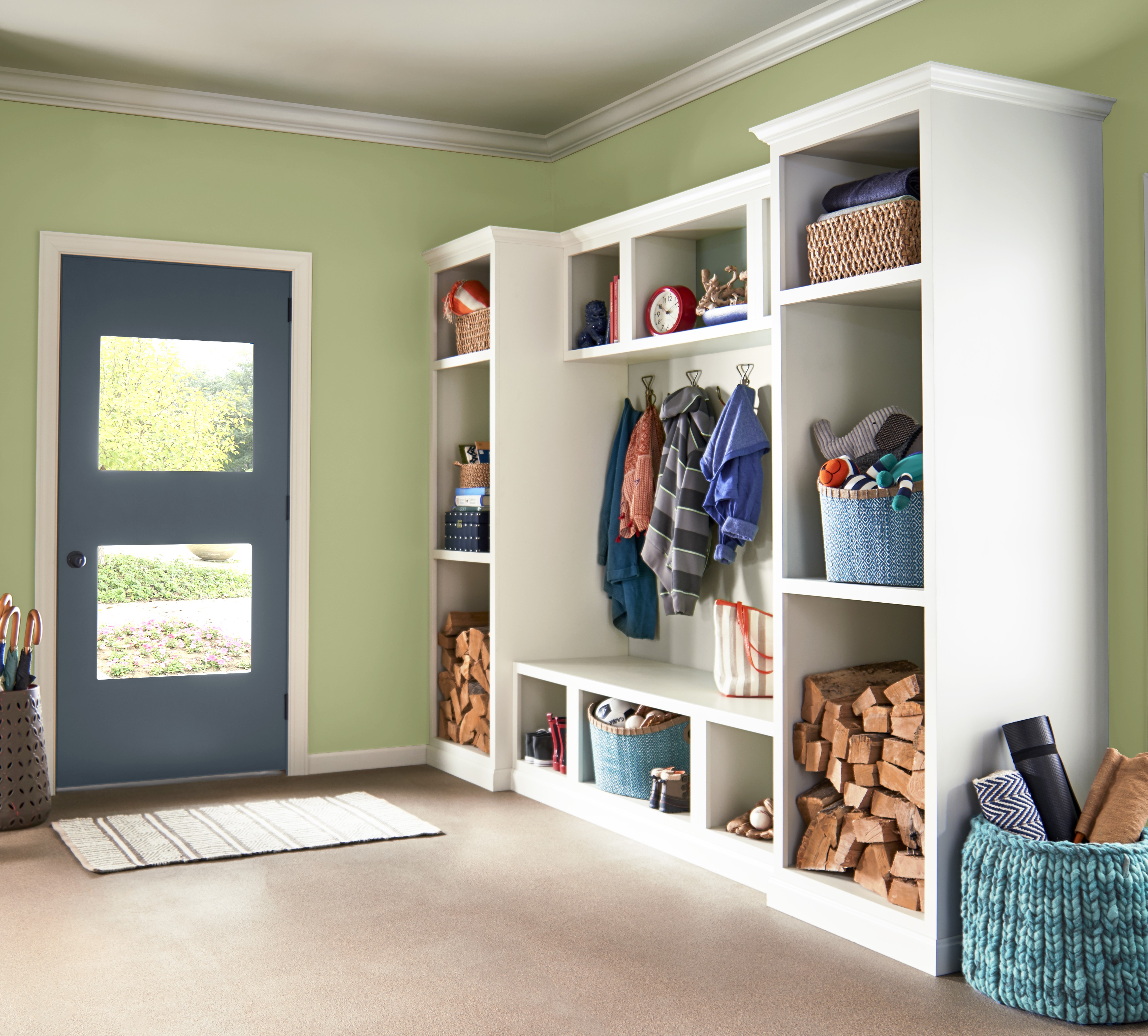 A room with walls painted in Sweet Grass, a soft green hue. The trim and ceiling are in Arid Landscape, a warm beige, while the door stands out in Midnight Blue, adding a bold contrast.