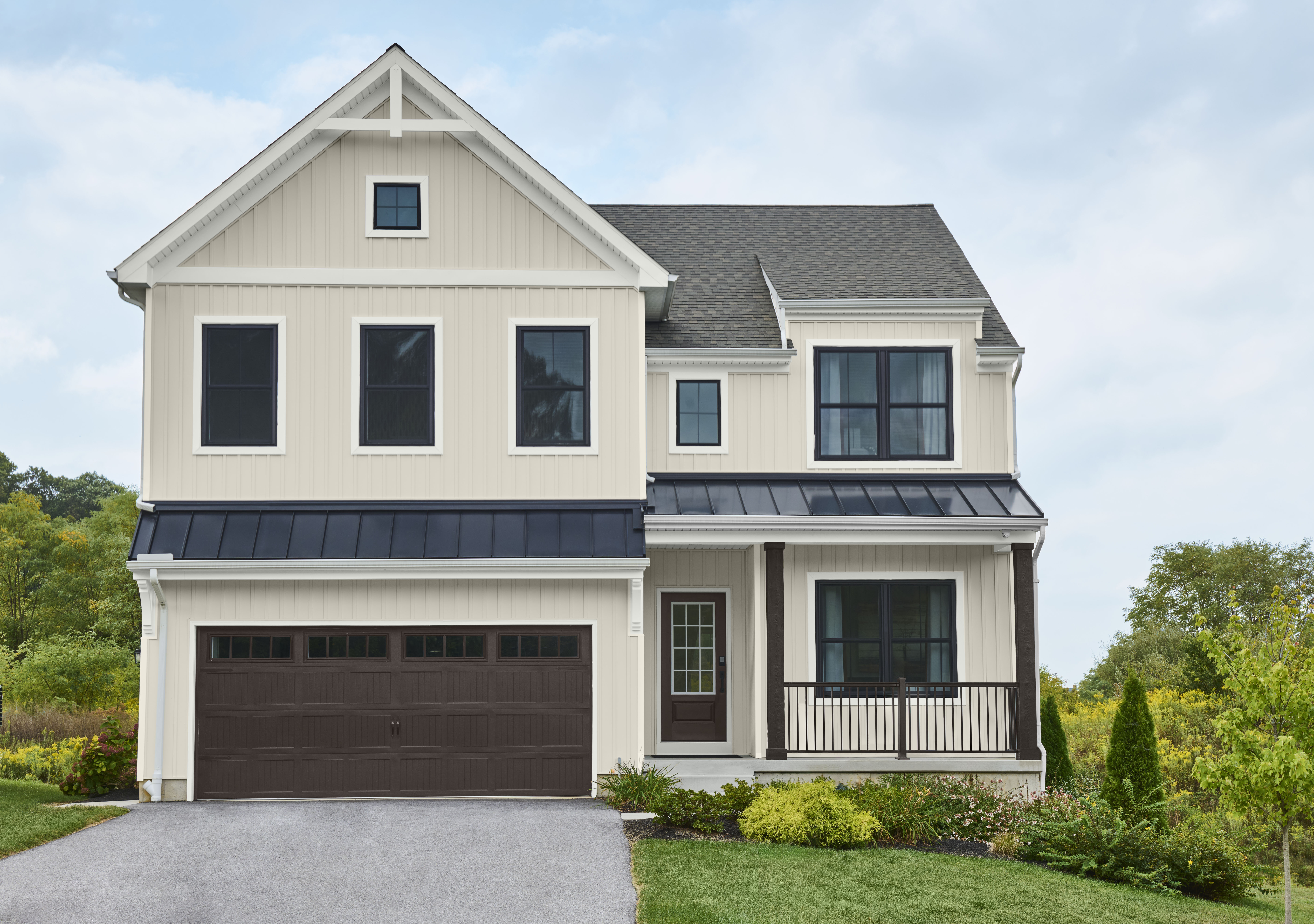 A small, two-story farmhouse with a dark brown garage door, and dark brown porch columns and rails. The house is painted in a soft off-white colour called Blank Canvas.