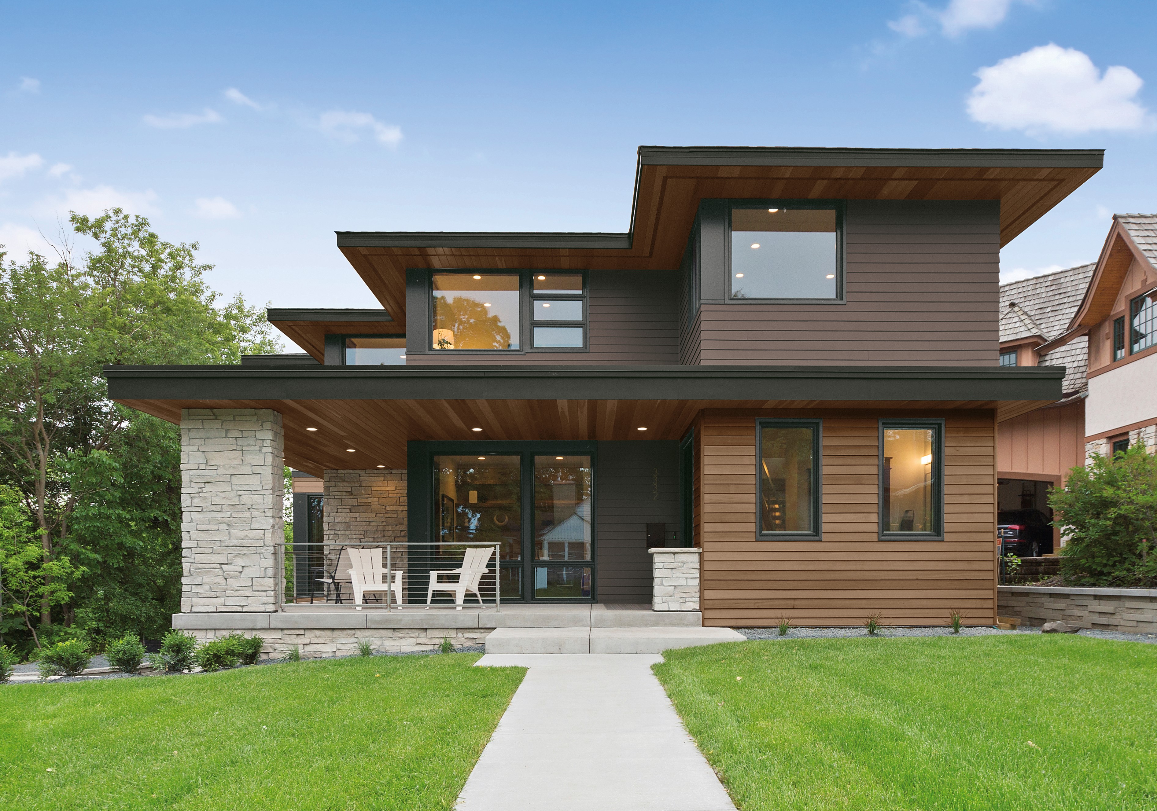 A large, two-story modern house with dark brown siding and soft black trim in the colour Cracked Pepper. The house features wood siding that adds a natural element and is complemented by a beautifully manicured green lawn.