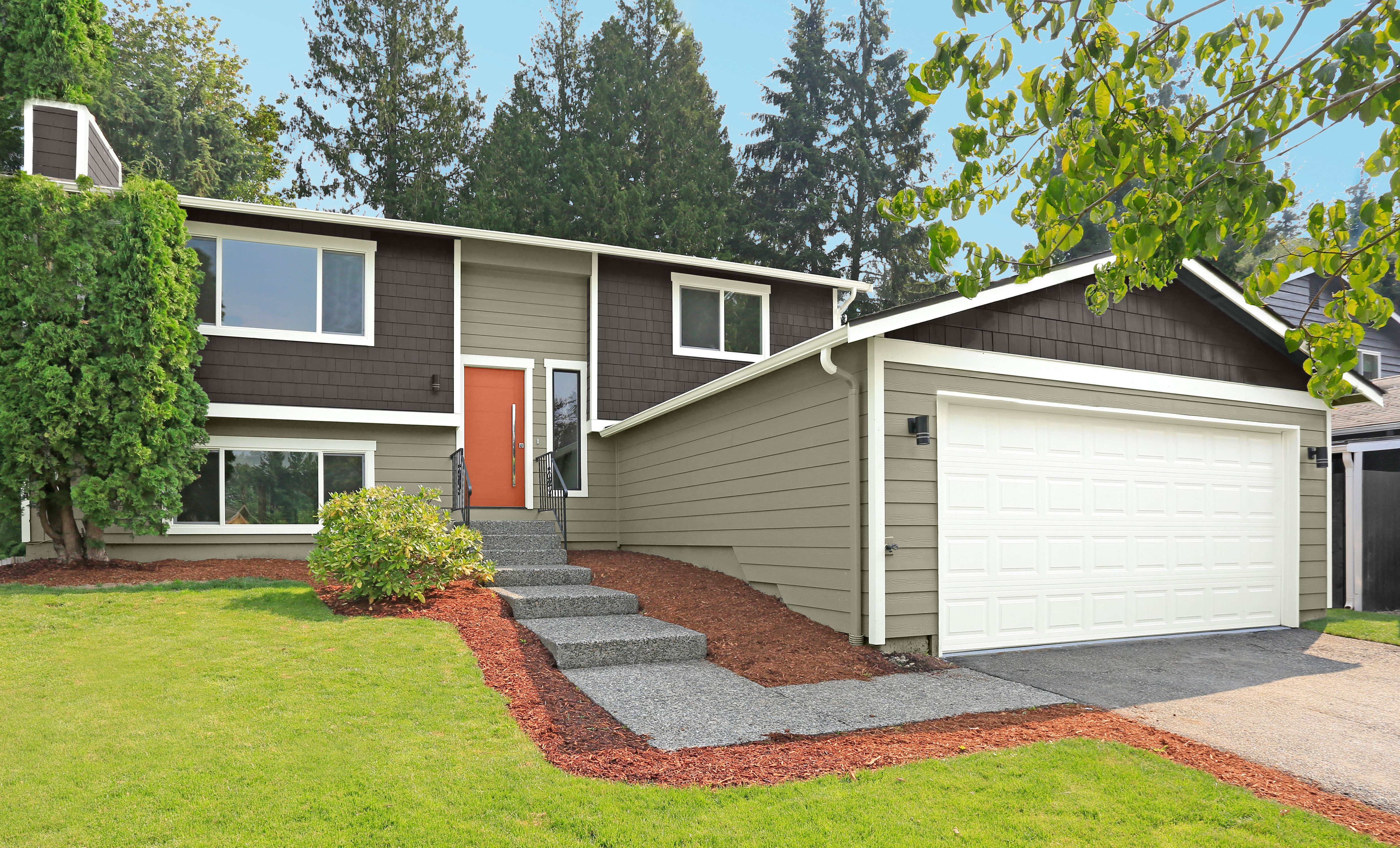 A two-story ranch-style house with siding, painted in two tones of camo green and dark brown. The front door is orange, giving the house a modern look.