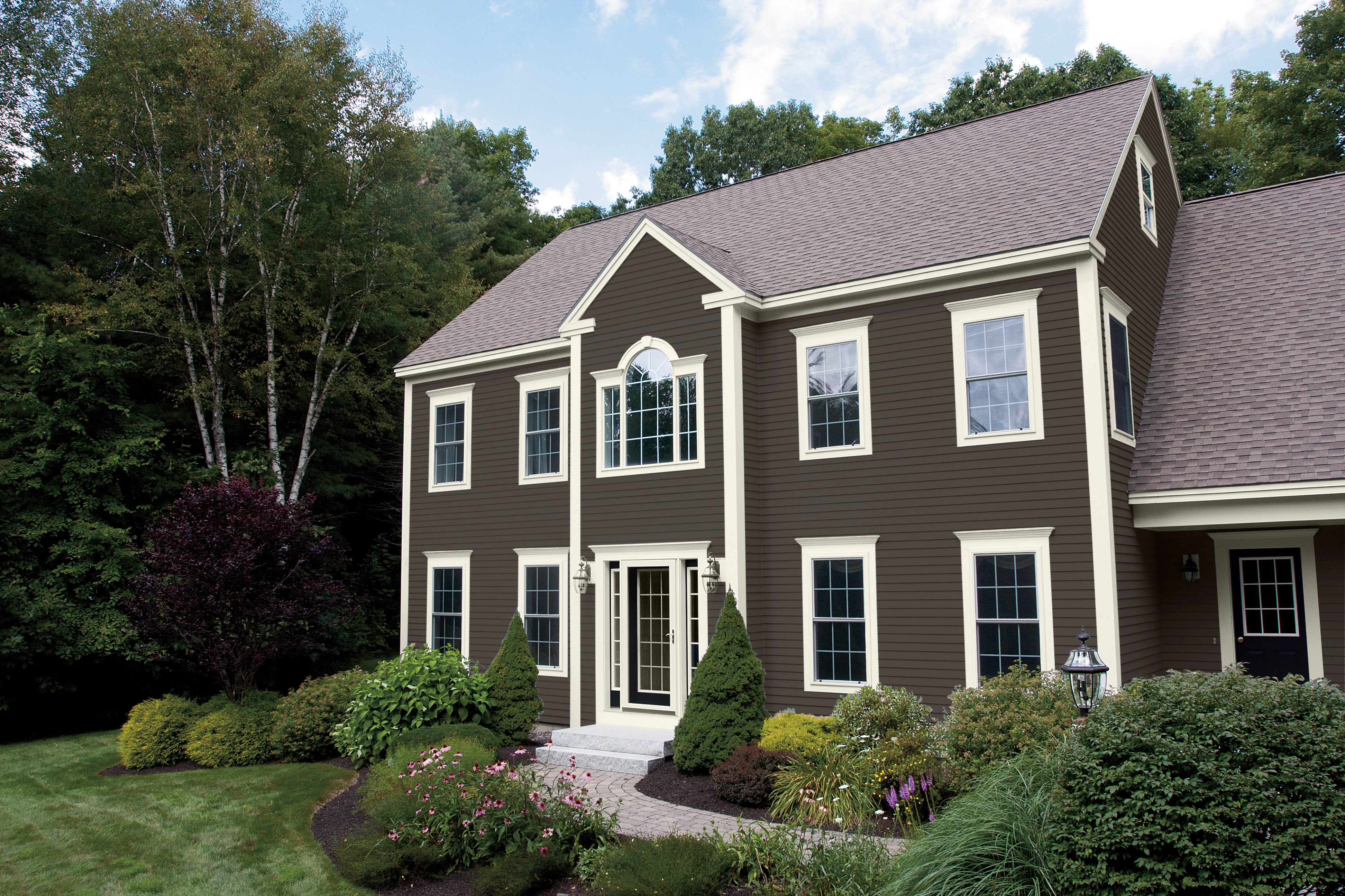 A colonial-style home painted in a rich dark chocolate brown colour. The house features crisp white trim around the windows and edges, with striking black doors that add a touch of elegance. The overall appearance is classic and sophisticated.