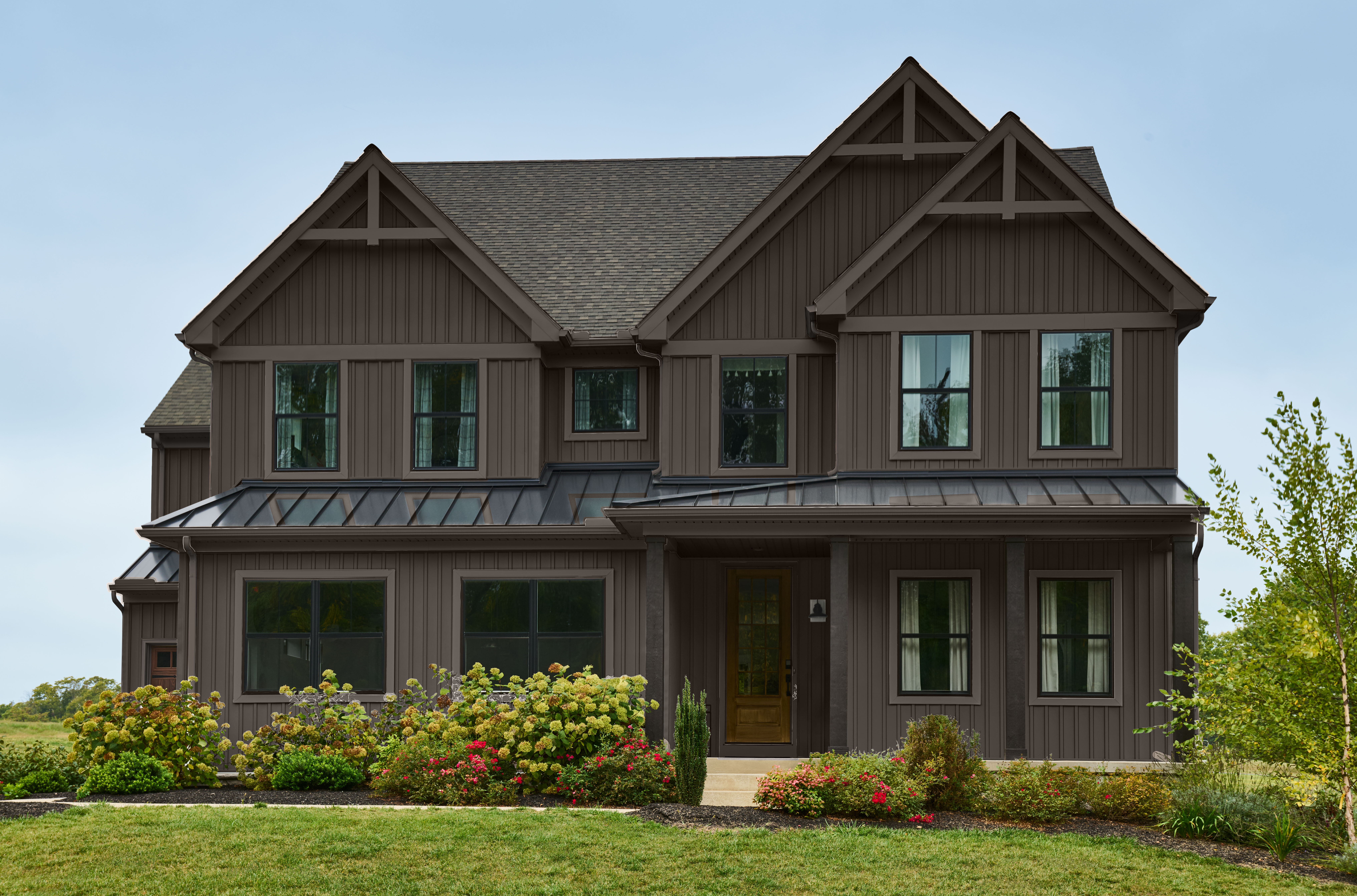 A two-story modern Craftsman-style home, drenched in a dark brown paint colour. There are three roof pitches add character and visual interest to the roof lines. 