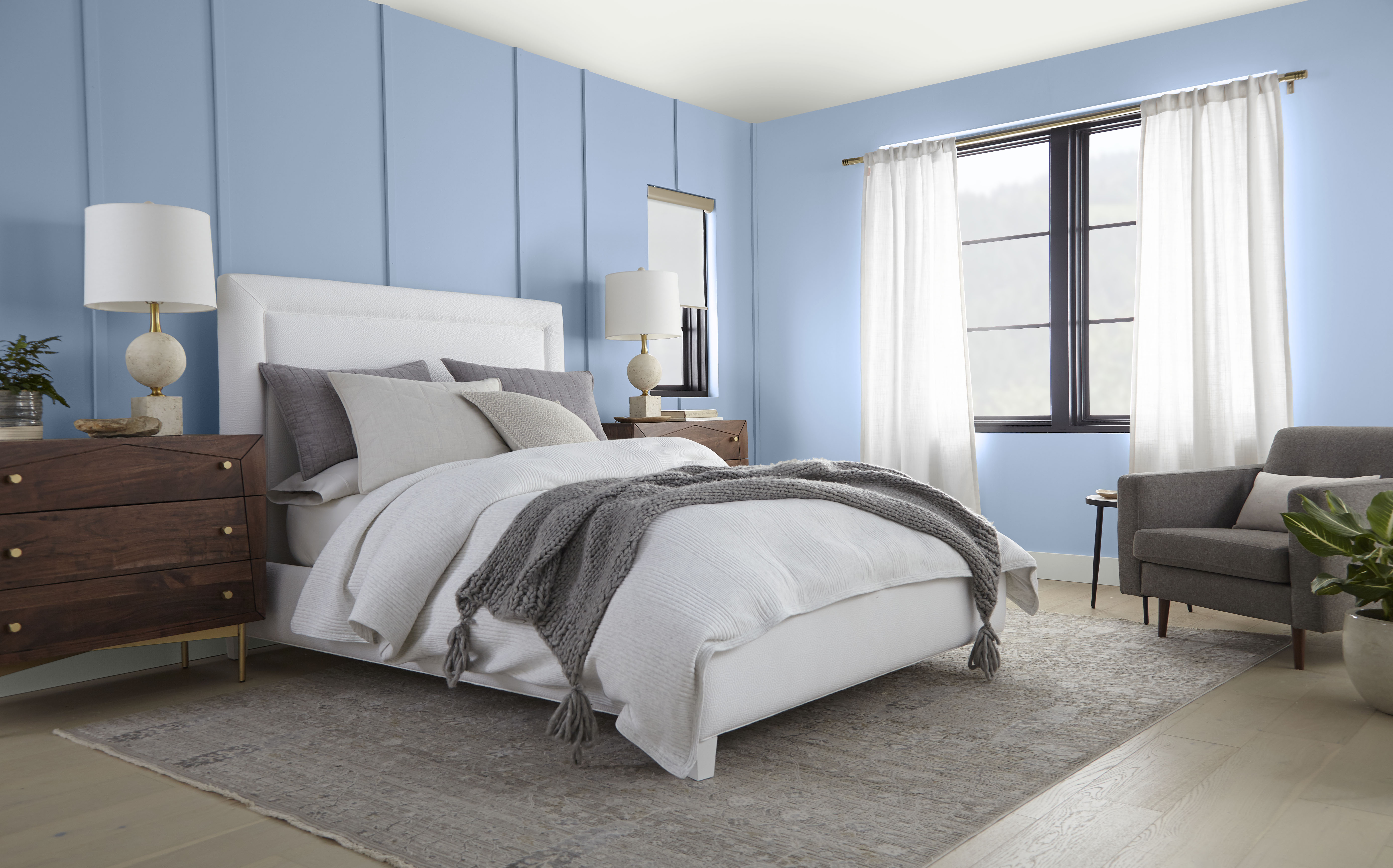 A serene bedroom with light blue walls, a comfortable bed adorned with neutral bedding, and light, sheer window coverings that allow natural light to gently filter in.