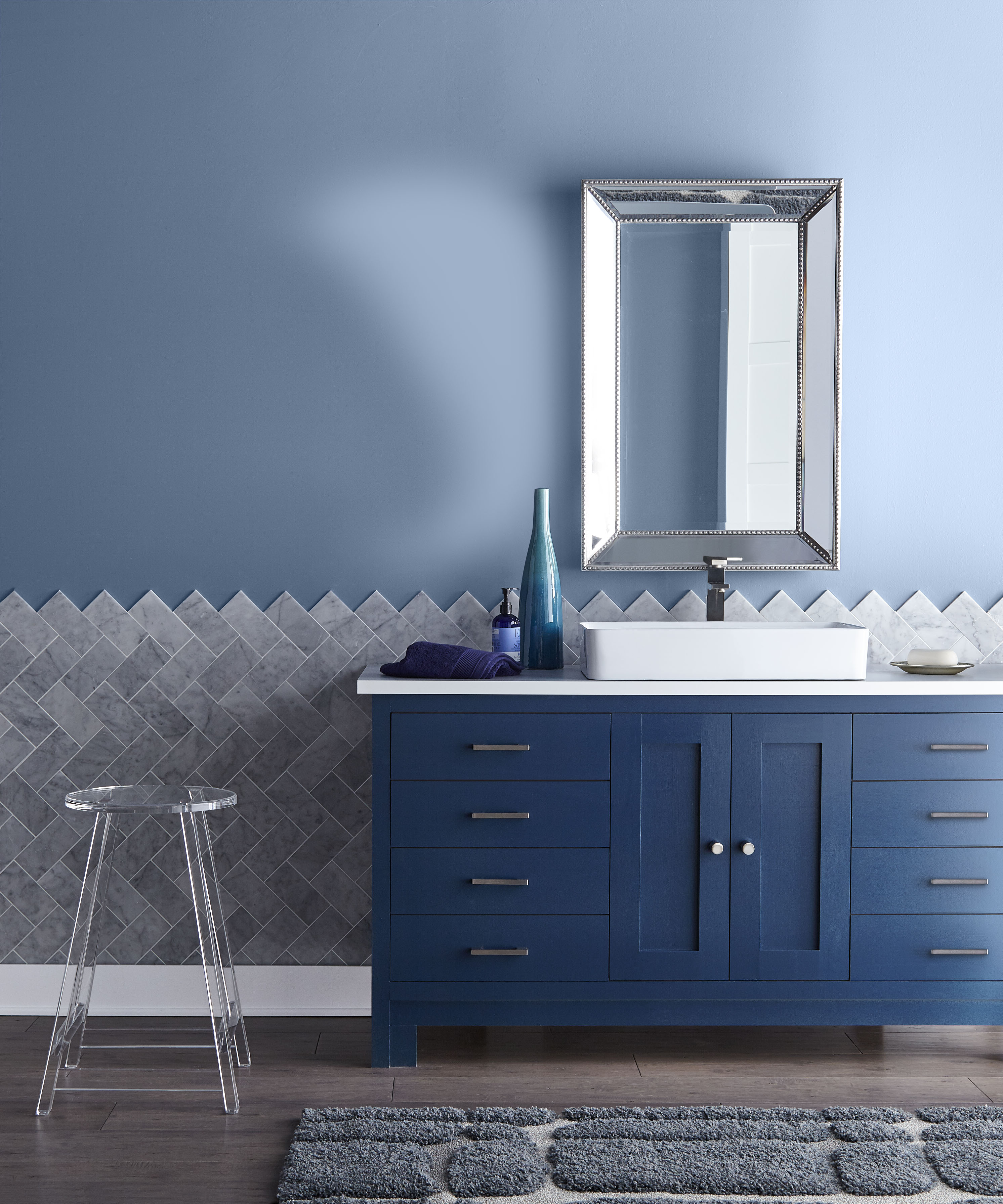 - A bathroom with the upper walls painted in a calming blue and the lower portion tiled with sleek grey tiles. The vanity is a striking dark blue, adding a touch of elegance to the space