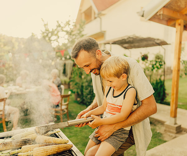 A dad and his son grilling corn on the cob.